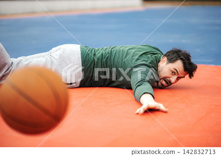 Man falling on basketball court reaching for ball 142832713