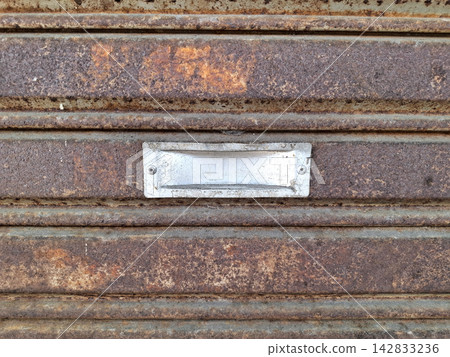 Silver metal handle plate secured on decaying rusted steel shutter surface showcasing industrial architectural details and textures. Silver metal handle plate secured on decaying rusted steel shutter surface showcasing industrial architectural details and textures. 142833236