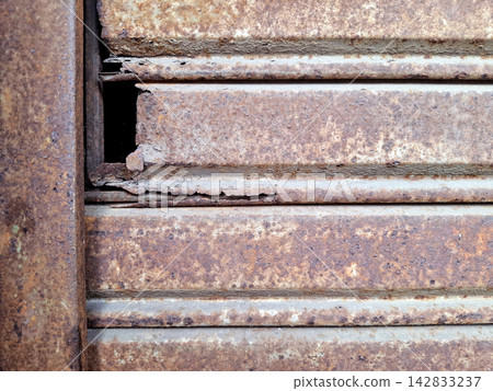 Rusted metal shutter surface featuring decaying iron texture and structural damage ideal for industrial backgrounds and grungy architectural designs. Rusted metal shutter surface featuring decaying iron texture and structural damage ideal for industrial backgrounds and grungy architectural designs. 142833237