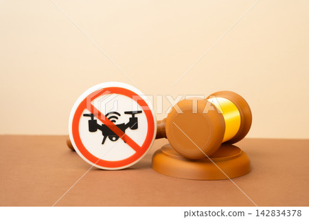 A drone ban symbol and a judge's gavel. Tightening laws against unmanned systems and vehicles. Concept of aviation regulation and airspace security policy. Tighter oversight. 142834378