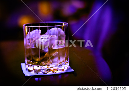 在黑暗中,紫色燈光照亮了盛在岩石杯中的威士忌。 在黑暗中,紫色燈光照亮了盛在岩石杯中的威士忌。 142834505