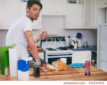 Man, portrait and eating with breakfast in kitchen for morning meal, snack or food at home. Young male person with sandwich, bread or wheat for healthy nutrition, fiber or start of day at house 142834592