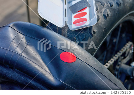 A person is applying a red patch to a bicycle tire using a repair kit on a sunny day in an outdoor setting A person is applying a red patch to a bicycle tire using a repair kit on a sunny day in an outdoor setting 142835130