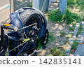 A bicycle is parked on a sidewalk with a flat rear tire. Grass grows nearby under clear skies. The setting is typical for an urban area 142835141