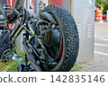 A bike is secured at a parking spot in an urban area. The bike shows a close-up view of the rear wheel and gear system, with grass nearby 142835146