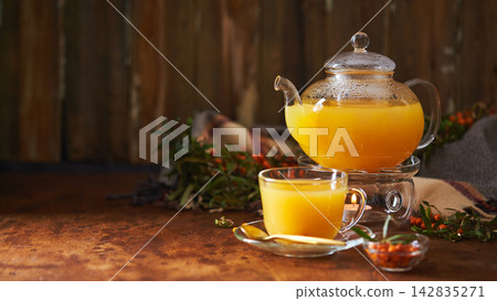 Glass teapot and sea buckthorn tea cup on wooden background Glass teapot and sea buckthorn tea cup on wooden background 142835271
