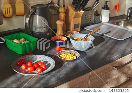 Sunliht modern kitchen with plate of quinoa filled with vegetables and ingredients on the countertop. Sunliht modern kitchen with plate of quinoa filled with vegetables and ingredients on the countertop. 142835295
