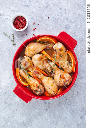 Chicken drumsticks with oranges and thyme baked in red round baking dish Chicken drumsticks with oranges and thyme baked in red round baking dish 142835306