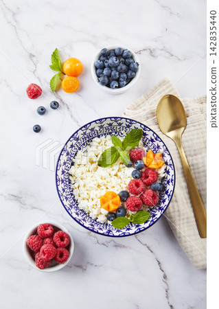 Cottage cheese in bowl garnished with raspberries, blueberries, physalis and mint leaves on white background Cottage cheese in bowl garnished with raspberries, blueberries, physalis and mint leaves on white background 142835440