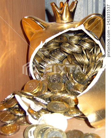 Extreme close-up of a broken golden piggy bank overflowing with shiny metal coins, representing wealth, savings, and financial concepts. Extreme close-up of a broken golden piggy bank overflowing with shiny metal coins, representing wealth, savings, and financial concepts. 142835537