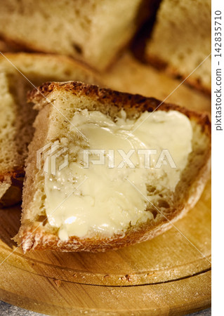 Fresh rustic bread slice with butter on wooden cutting board 142835710