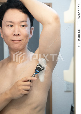A man grooming his underarm hair at the bathroom sink at home. 142835868