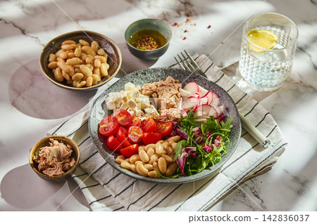 Healthy tuna salad bowl with white beans, feta cheese, tomatoes, radish, and greens on marble table Healthy tuna salad bowl with white beans, feta cheese, tomatoes, radish, and greens on marble table 142836037
