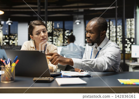 Team of office clerks completing spreadsheets on laptop, analyzing data, brainstorming. Teamworking colleagues browsing internet on notebook, researching information online, working overnight 142836161