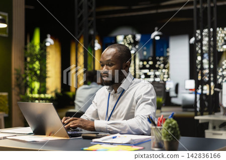 Worker typing on laptop keyboard at office desk, doing computer tasks, working overnight. African american man using notebook at work, researching key data for company project Worker typing on laptop keyboard at office desk, doing computer tasks, working overnight. African american man using notebook at work, researching key data for company project 142836166
