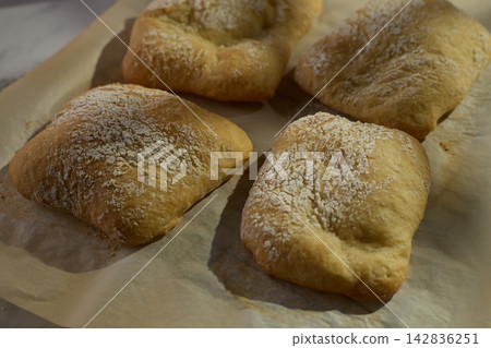 Close-up of homemade mini ciabatta rolls dusted with flour on parchment paper Close-up of homemade mini ciabatta rolls dusted with flour on parchment paper 142836251