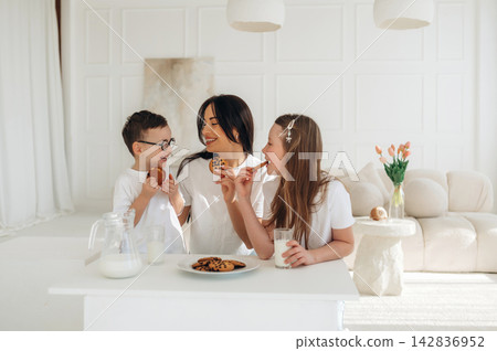 Family enjoying cookies and milk together at a bright kitchen table with a plate of cookies and a glass of milk in a modern, minimalist interior setting Family enjoying cookies and milk together at a bright kitchen table with a plate of cookies and a glass of milk in a modern, minimalist interior setting 142836952