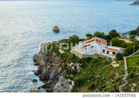 Stunning coastal landscape featuring a modern Mediterranean house surrounded by lush greenery and blue water Stunning coastal landscape featuring a modern Mediterranean house surrounded by lush greenery and blue water 142837098