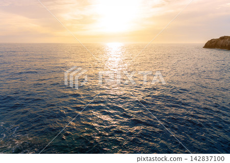 Tranquil ocean horizon view with warm sunlight glistening across the gentle evening waves Tranquil ocean horizon view with warm sunlight glistening across the gentle evening waves 142837100