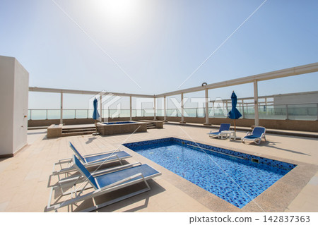 Rooftop pool area with lounge chairs and clear sky in a city setting during midday Rooftop pool area with lounge chairs and clear sky in a city setting during midday 142837363