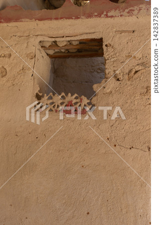 Old wall with a small opening showing decorative work in a historical building in a desert area during the day Old wall with a small opening showing decorative work in a historical building in a desert area during the day 142837389