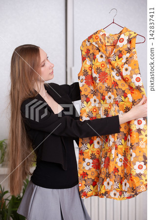 Woman holding a bright dress in a room with plants and light colors during the day Woman holding a bright dress in a room with plants and light colors during the day 142837411