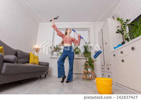 Woman dances while cleaning her home in a bright apartment during the day with plants around her Woman dances while cleaning her home in a bright apartment during the day with plants around her 142837427