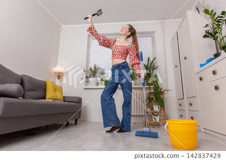 Woman holds a paint roller while standing in a bright room with plants and cleaning tools Woman holds a paint roller while standing in a bright room with plants and cleaning tools 142837429