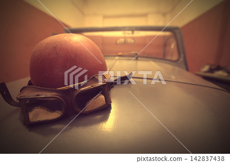Vintage helmet and goggles on a classic car in a dim garage setting in the early morning hours Vintage helmet and goggles on a classic car in a dim garage setting in the early morning hours 142837438
