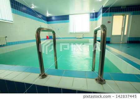 Indoor swimming pool with bright tiles and clear water, located in a wellness center during afternoon light Indoor swimming pool with bright tiles and clear water, located in a wellness center during afternoon light 142837445