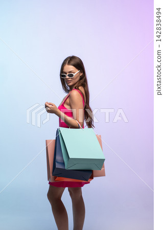 Woman fashionably dressed, holding multiple shopping bags, posing stylishly after a successful shopping spree 142838494