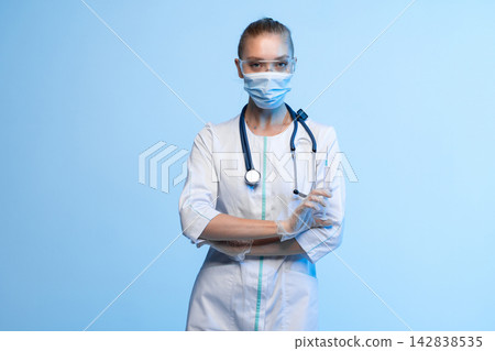 Healthcare professional in mask, goggles, and stethoscope holding syringe, symbolizing vaccination and medicine Healthcare professional in mask, goggles, and stethoscope holding syringe, symbolizing vaccination and medicine 142838535