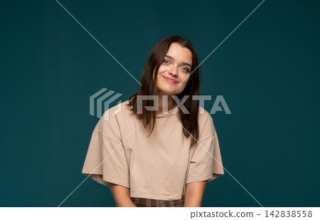 Young brunette woman with a casual smile and happy expression posing on a teal studio background Young brunette woman with a casual smile and happy expression posing on a teal studio background 142838558