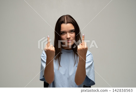 Young woman showing middle fingers at camera, expressing frustration and defiance with offensive gesture Young woman showing middle fingers at camera, expressing frustration and defiance with offensive gesture 142838563
