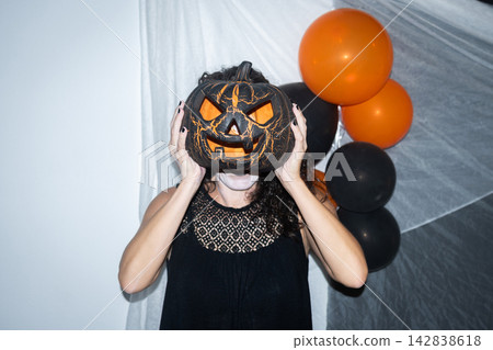 Woman hiding her face behind a Halloween pumpkin Woman hiding her face behind a Halloween pumpkin 142838618