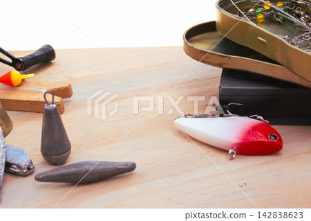 Fishing gear laid out on a wooden background: red-and-white lure, lead weights, bobber and open tackle box with hooks, swivels and pliers for an angling setup Fishing gear laid out on a wooden background: red-and-white lure, lead weights, bobber and open tackle box with hooks, swivels and pliers for an angling setup 142838623