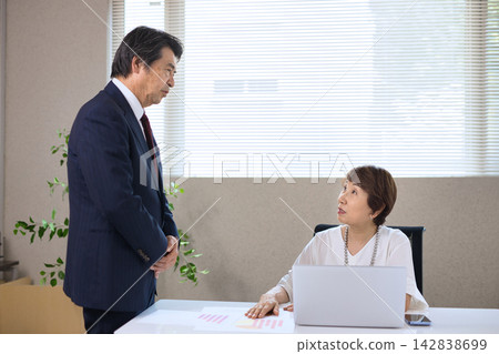 A businessman and businesswoman in their 60s having a meeting in the office. A businessman and businesswoman in their 60s having a meeting in the office. 142838699