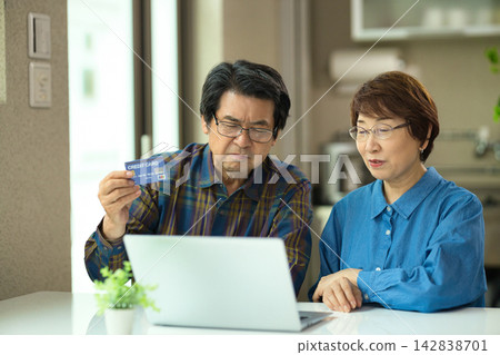 A senior couple enters credit card information while looking at a computer. A senior couple enters credit card information while looking at a computer. 142838701