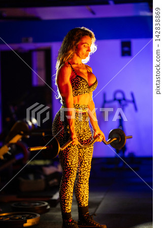 Strong person lifts weights in a gym with bright lighting and dark background during evening workout session Strong person lifts weights in a gym with bright lighting and dark background during evening workout session 142838869