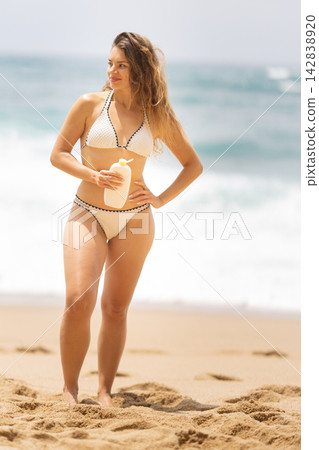 Woman stands on sandy beach holding drink while ocean waves crash in the background during sunny day Woman stands on sandy beach holding drink while ocean waves crash in the background during sunny day 142838920
