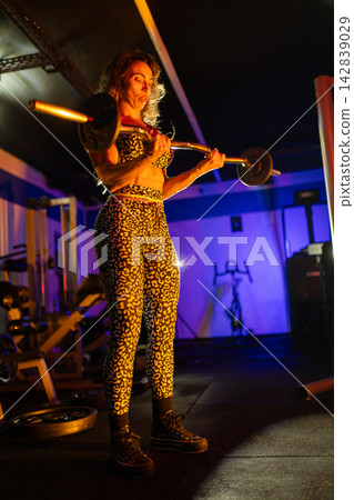 Woman lifting weights in gym during evening workout session in a colorful atmosphere 142839029