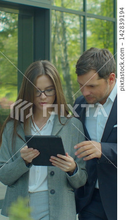 Vertical video. Business people going to work with digital tablet on street. Man and woman walking near office in morning. 142839194