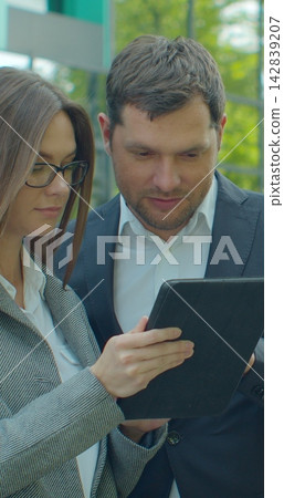 Vertical video. Business people standing near business center with digital tablet. Man and woman read news on Tablet Computer near office in morning. 142839207