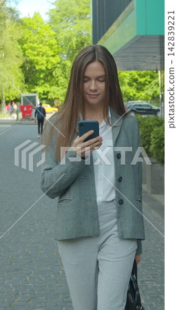 Vertical video. Caucasian businesswoman walking the street at the office center and talking on the phone. Close up. Rear. Outside. Vertical video. Caucasian businesswoman walking the street at the office center and talking on the phone. Close up. Rear. Outside. 142839221
