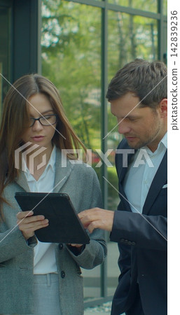 Vertical video. Business people going to work with digital tablet on street. Man and woman walking near office in morning. Vertical video. Business people going to work with digital tablet on street. Man and woman walking near office in morning. 142839236