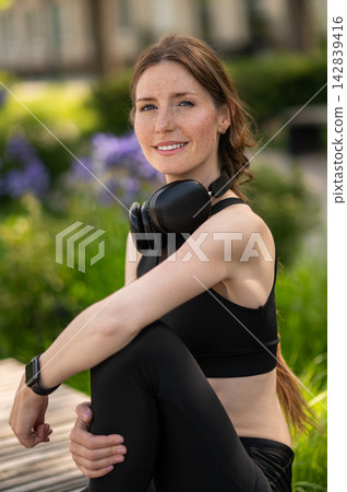 Woman in black sportswear sitting on a bench in a the park Woman in black sportswear sitting on a bench in a the park 142839416
