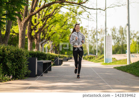 Young slim woman running on a greenery background Young slim woman running on a greenery background 142839462