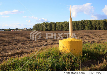 Gas pipeline marker post standing in a ploughed farm field 142839510