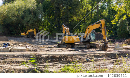 Yellow excavators are carrying out earthworks to create a recreation area, involving soil movement, site preparation, and landscaping. Yellow excavators are carrying out earthworks to create a recreation area, involving soil movement, site preparation, and landscaping. 142839511