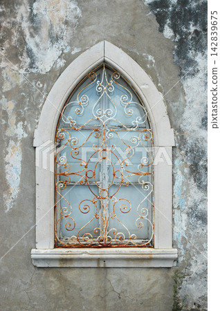Gothic pointed window with ornate rusty security grill Gothic pointed window with ornate rusty security grill 142839675